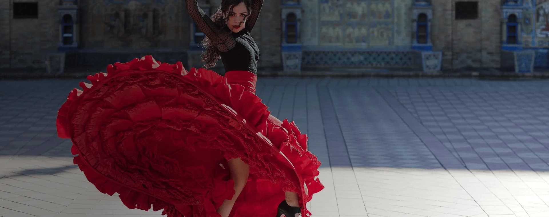Flamenco dancer twirls in front of grand building backdrop. Overlaid is the Spanish word "bailar" with its English translation, "to dance".