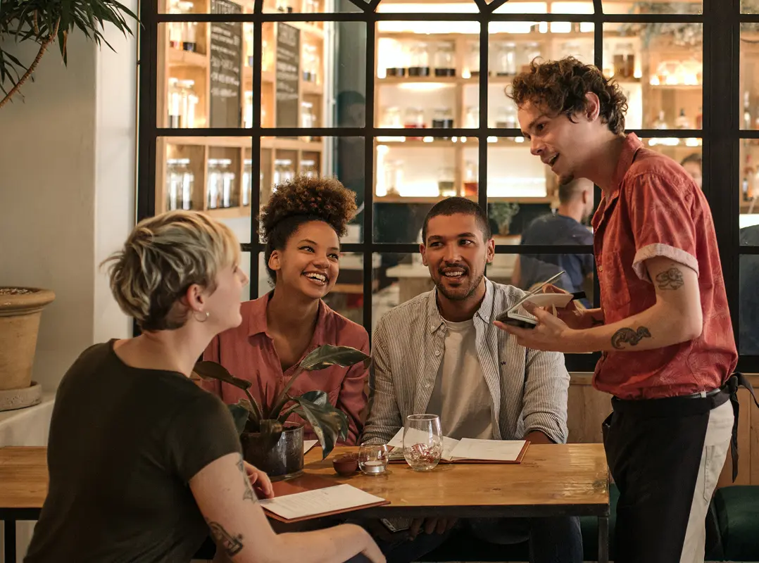 Group of friends practice a new language they have learned as they order from a waiter in a stylish cafe.