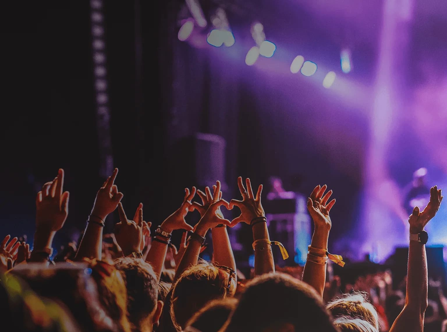 Crowd raises hands in excitement at live music performance. Overlaid is the German word "Konzert" with its English translation, "concert".