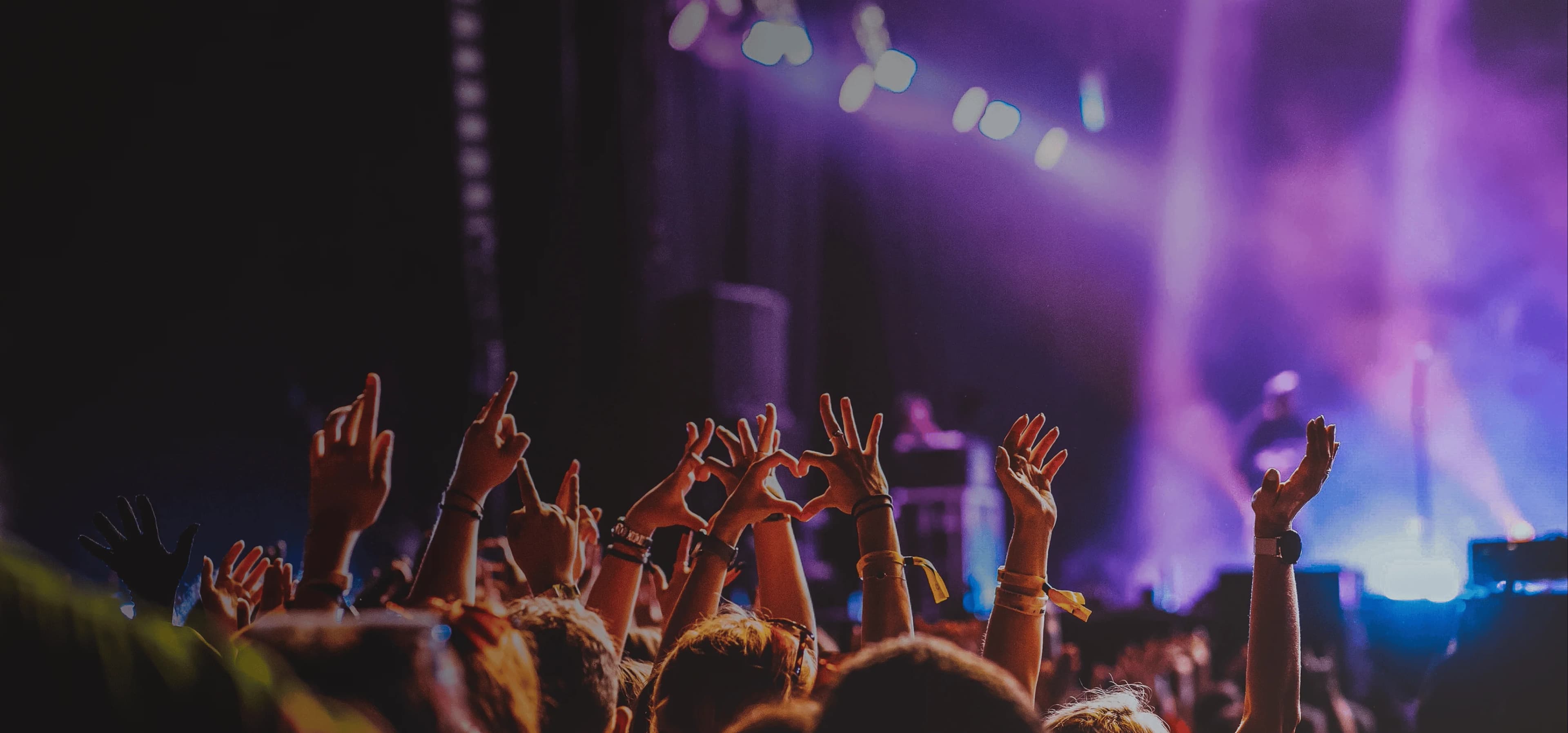 Crowd raises hands in excitement at live music performance. Overlaid is the German word "Konzert" with its English translation, "concert".